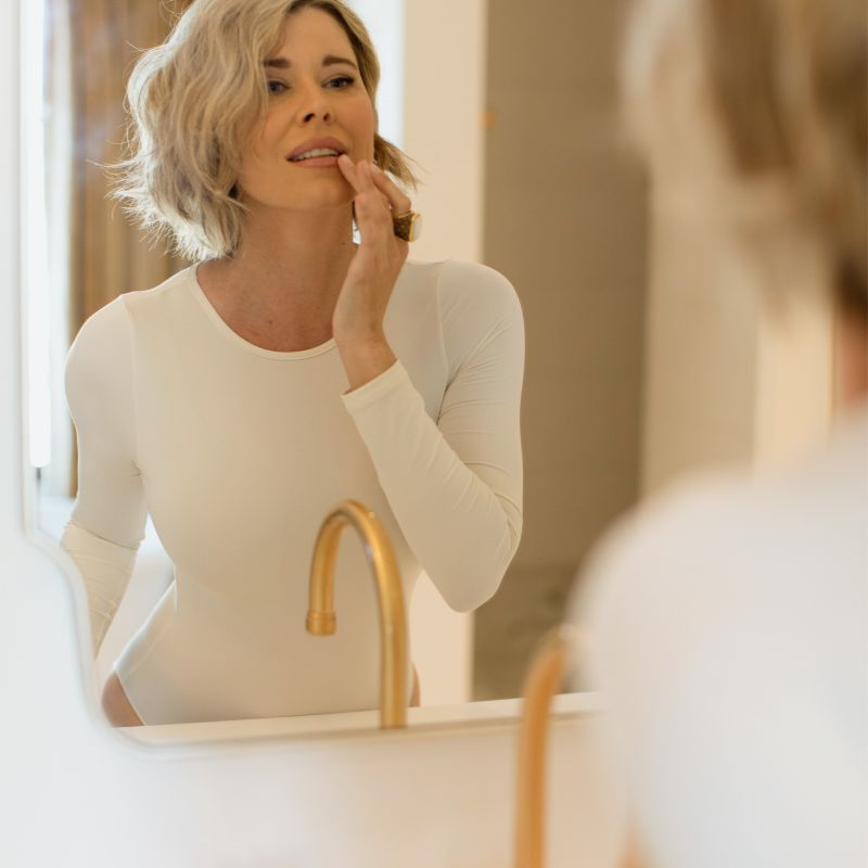 Beautiful Women looking in mirror wearing an Adea Long Sleeve Bodysuit in Off-white.